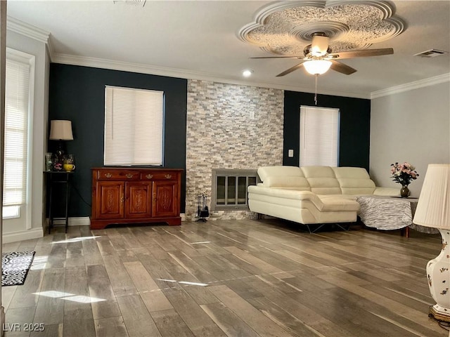 living room featuring hardwood / wood-style flooring, ceiling fan, a stone fireplace, and ornamental molding