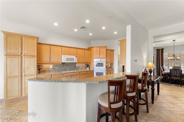 kitchen with white appliances, backsplash, a kitchen breakfast bar, a notable chandelier, and light stone countertops