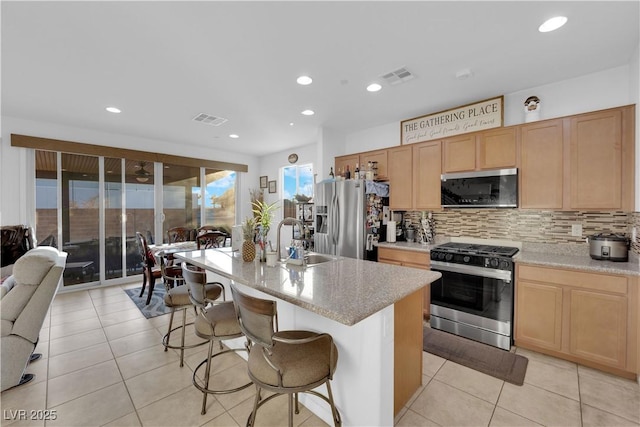 kitchen featuring sink, backsplash, a kitchen bar, a center island with sink, and appliances with stainless steel finishes