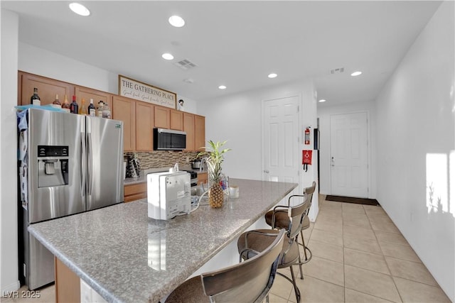 kitchen featuring light stone countertops, a center island, stainless steel fridge, decorative backsplash, and light tile patterned floors