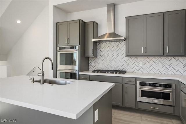 kitchen with tasteful backsplash, a kitchen island with sink, stainless steel appliances, and wall chimney range hood