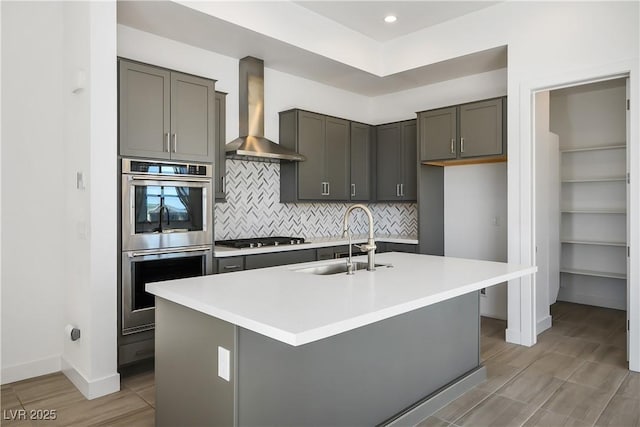 kitchen with gas stovetop, a sink, decorative backsplash, double oven, and wall chimney range hood