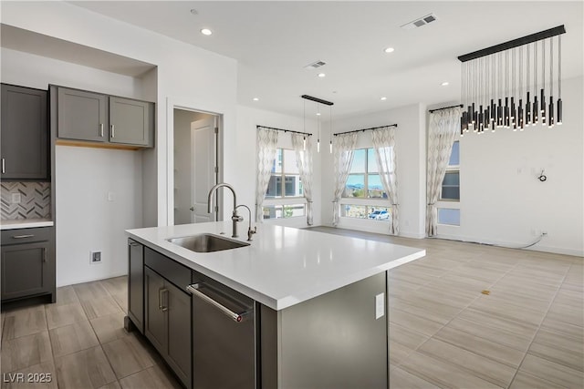 kitchen with gray cabinetry, sink, hanging light fixtures, decorative backsplash, and a center island with sink