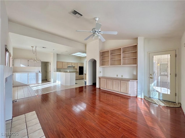 unfurnished living room with ceiling fan with notable chandelier, light wood-type flooring, and lofted ceiling