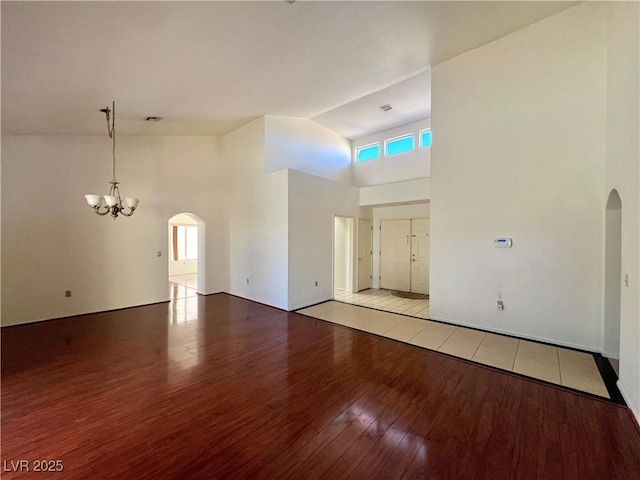 unfurnished room with high vaulted ceiling, light wood-type flooring, and an inviting chandelier