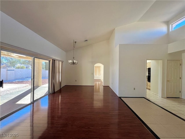 empty room with tile patterned floors, a healthy amount of sunlight, high vaulted ceiling, and a chandelier