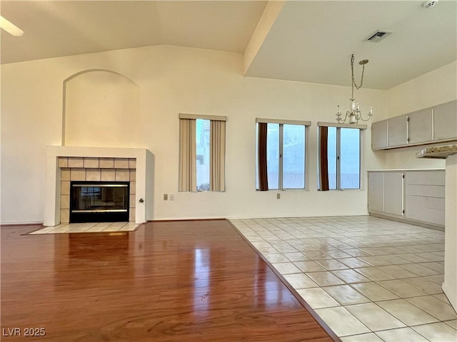 3012 Morning Ridge Dr, Las Vegas, NV 89134 - unfurnished living room featuring lofted ceiling, plenty of natural light, a chandelier, a tiled fireplace, and light wood-style flooring