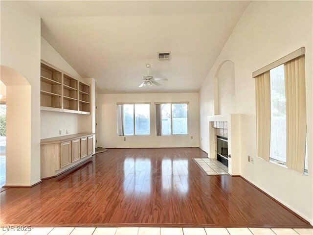 unfurnished living room featuring light hardwood / wood-style flooring, vaulted ceiling, ceiling fan, and a tiled fireplace