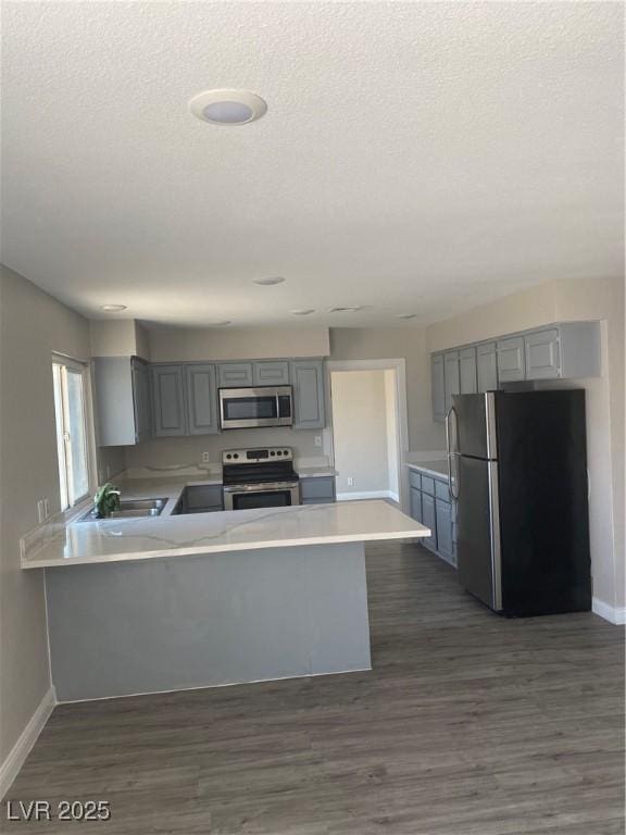 kitchen with sink, dark hardwood / wood-style flooring, kitchen peninsula, gray cabinets, and appliances with stainless steel finishes