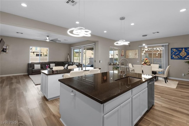 kitchen with sink, white cabinetry, decorative light fixtures, stainless steel dishwasher, and a kitchen island with sink