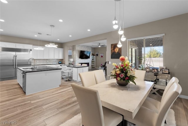 dining space with ceiling fan, sink, light wood-type flooring, and a large fireplace