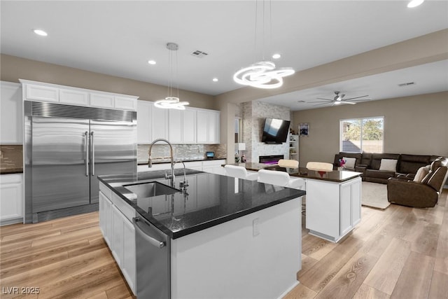 kitchen featuring an island with sink, decorative light fixtures, sink, built in refrigerator, and white cabinets