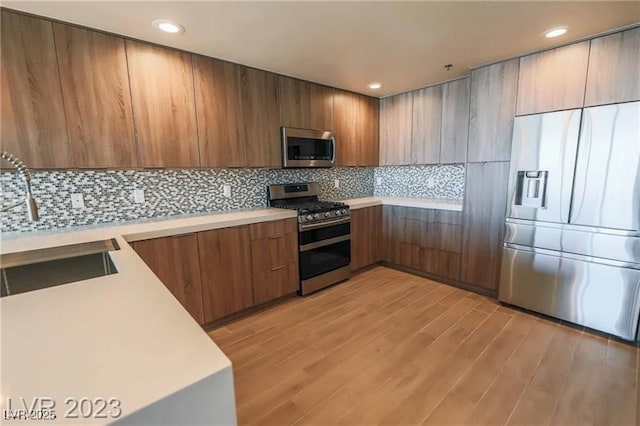 kitchen featuring stainless steel appliances, light hardwood / wood-style flooring, tasteful backsplash, and sink