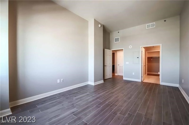 unfurnished bedroom featuring a towering ceiling, a walk in closet, dark hardwood / wood-style floors, and a closet