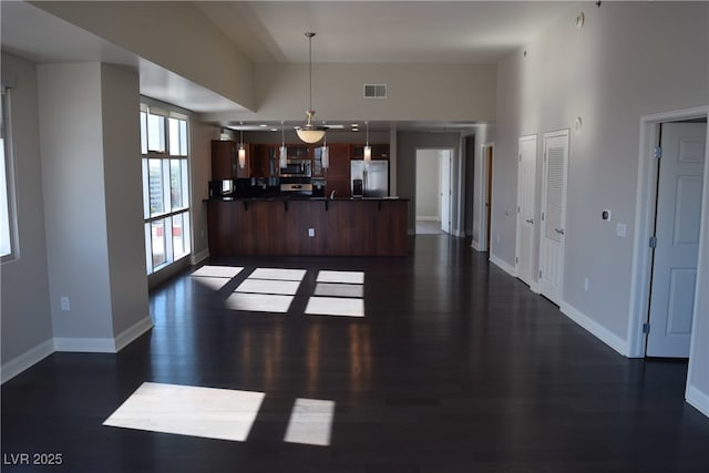 kitchen featuring kitchen peninsula, stainless steel appliances, hanging light fixtures, and dark wood-type flooring