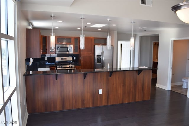 kitchen featuring dark wood-type flooring, pendant lighting, stainless steel appliances, and a kitchen breakfast bar