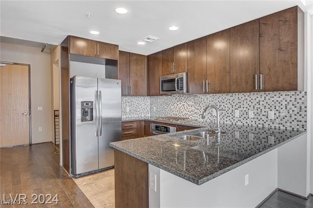 kitchen with sink, stainless steel appliances, tasteful backsplash, dark stone countertops, and kitchen peninsula