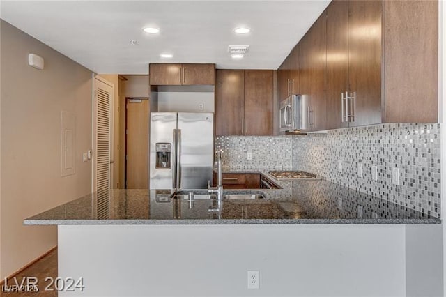 kitchen featuring kitchen peninsula, tasteful backsplash, dark stone counters, stainless steel appliances, and sink