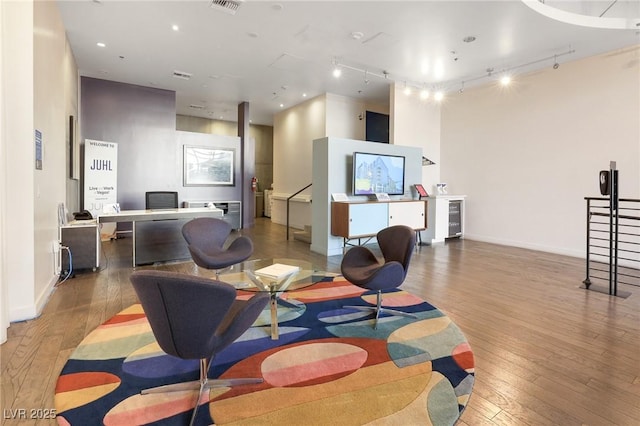 living room with wine cooler, wood-type flooring, a high ceiling, and track lighting