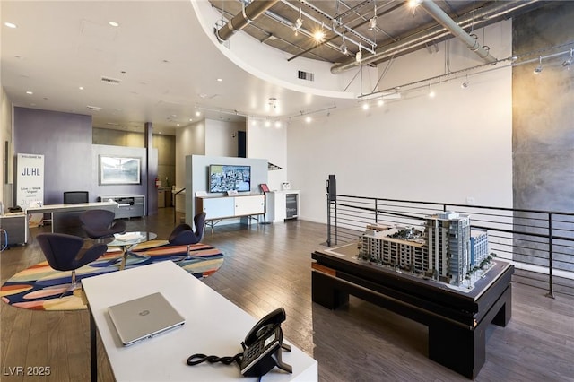 office space with dark hardwood / wood-style flooring, a towering ceiling, rail lighting, and beverage cooler