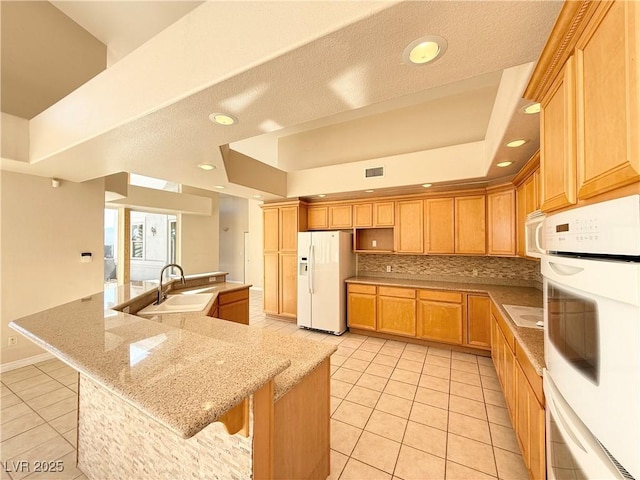 kitchen with white appliances, a kitchen breakfast bar, sink, light tile patterned floors, and light stone counters