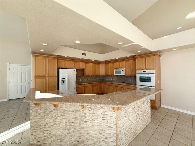 kitchen with a breakfast bar, light tile patterned floors, white appliances, and a spacious island