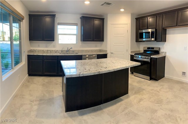 kitchen with light stone countertops, sink, a kitchen island, and appliances with stainless steel finishes