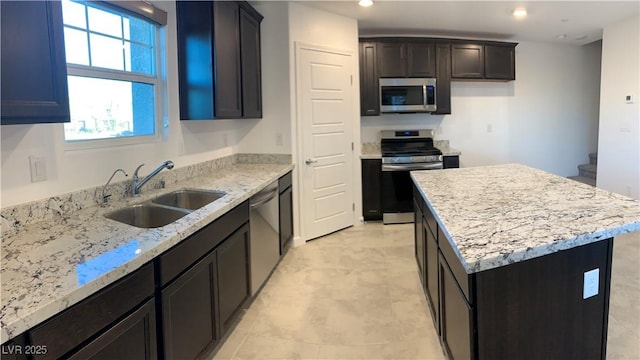 kitchen featuring light stone countertops, appliances with stainless steel finishes, a kitchen island, and sink