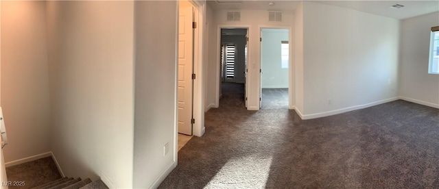 hallway featuring dark colored carpet and a healthy amount of sunlight