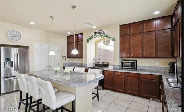 kitchen featuring a center island, light tile patterned floors, stainless steel appliances, and a breakfast bar area