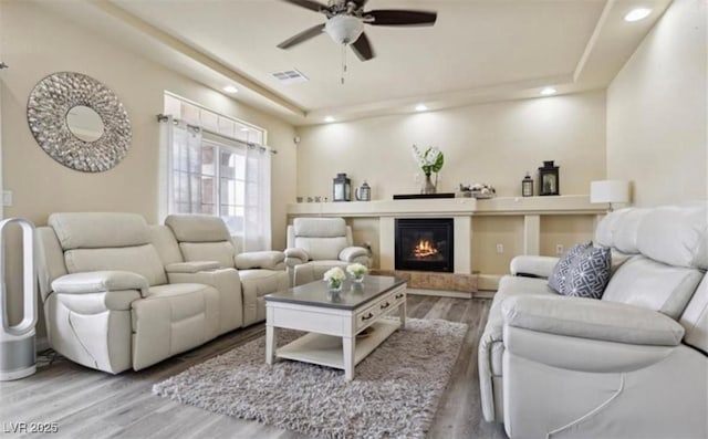 living room with hardwood / wood-style floors, a raised ceiling, and ceiling fan