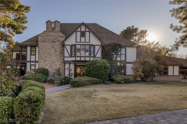 english style home with a balcony and a lawn