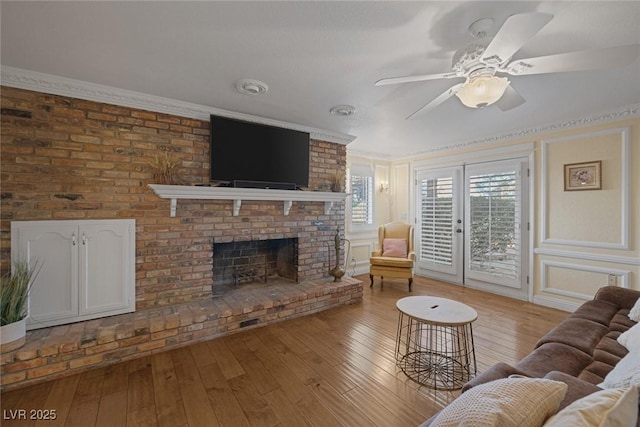 living room featuring a fireplace, french doors, ceiling fan, light hardwood / wood-style floors, and crown molding