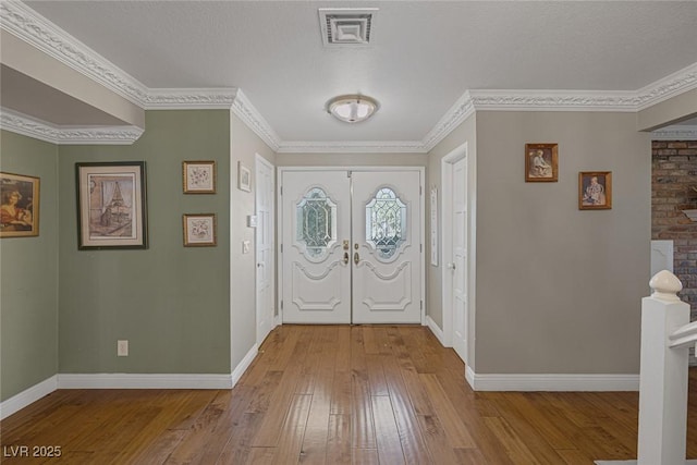 entrance foyer featuring french doors, a textured ceiling, ornamental molding, and light hardwood / wood-style flooring