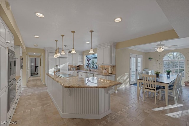 kitchen with decorative light fixtures, white cabinetry, a center island, ceiling fan, and light stone countertops