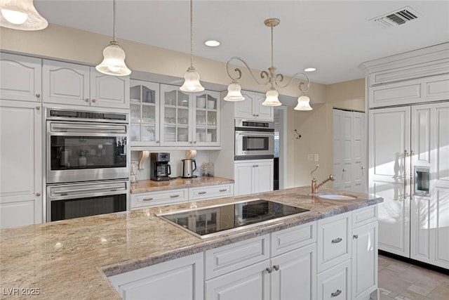 kitchen with black electric stovetop, double oven, white cabinets, decorative light fixtures, and sink