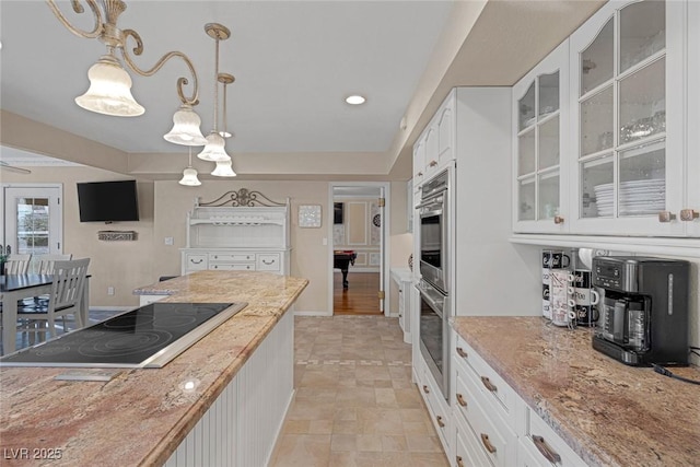 kitchen featuring white cabinets, black electric stovetop, pendant lighting, and light stone countertops