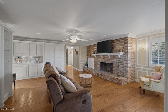 living room with a brick fireplace, ceiling fan, light hardwood / wood-style floors, and crown molding