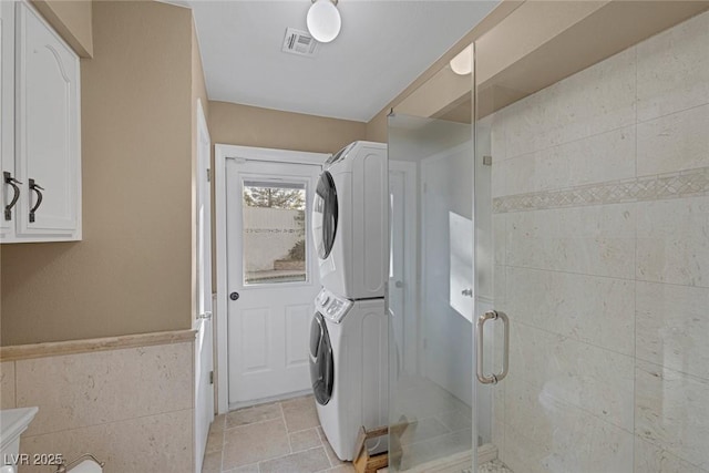 clothes washing area with tile walls and stacked washer / dryer