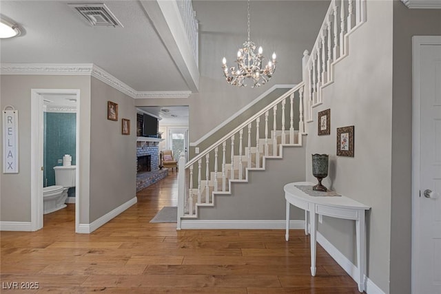 foyer with a brick fireplace, hardwood / wood-style floors, crown molding, and a notable chandelier