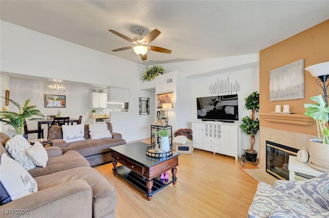 living room with a fireplace, light wood-type flooring, ceiling fan, and vaulted ceiling