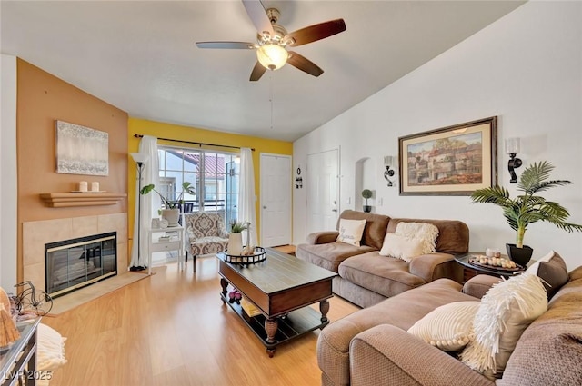 living room featuring a tiled fireplace, ceiling fan, light hardwood / wood-style floors, and lofted ceiling