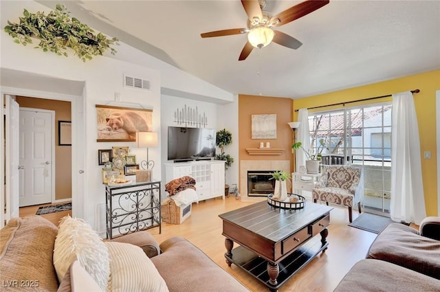 living room with ceiling fan, a tile fireplace, light hardwood / wood-style floors, and vaulted ceiling