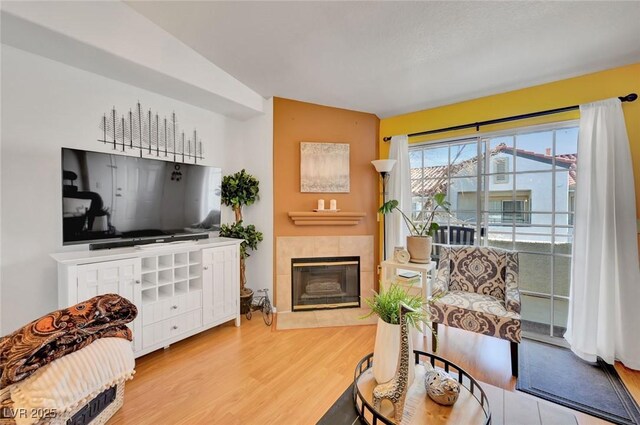 living room with light wood-type flooring, a tile fireplace, and vaulted ceiling