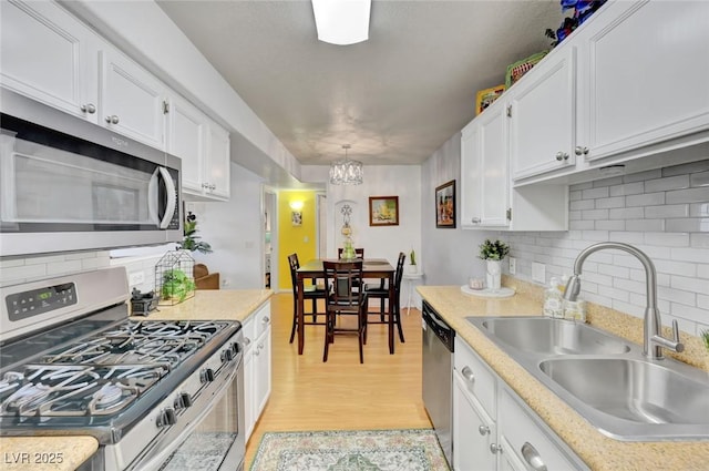 kitchen with sink, stainless steel appliances, white cabinets, and pendant lighting