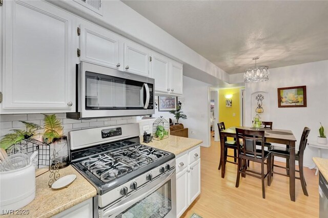 kitchen featuring decorative light fixtures, stainless steel appliances, white cabinetry, an inviting chandelier, and backsplash