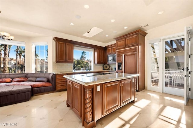 kitchen with decorative backsplash, black electric stovetop, light stone countertops, built in microwave, and a kitchen island