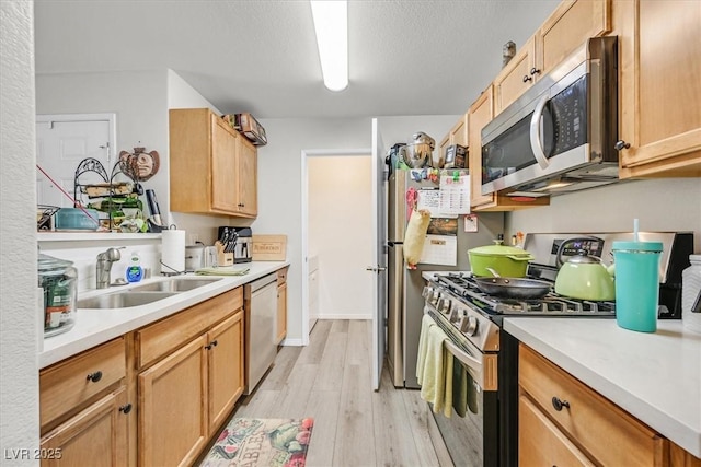 kitchen with a textured ceiling, sink, stainless steel appliances, and light hardwood / wood-style flooring