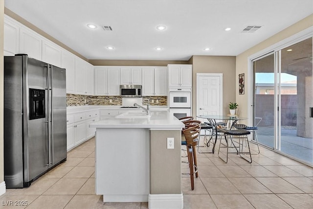 kitchen with decorative backsplash, stainless steel appliances, a center island with sink, white cabinets, and a breakfast bar area