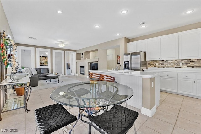 kitchen with white cabinetry, sink, stainless steel fridge, a center island with sink, and light tile patterned floors